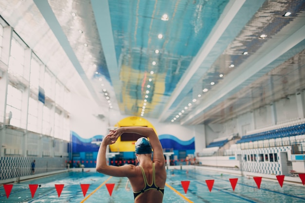 Young woman swimmer warming up before swim in swimming pool