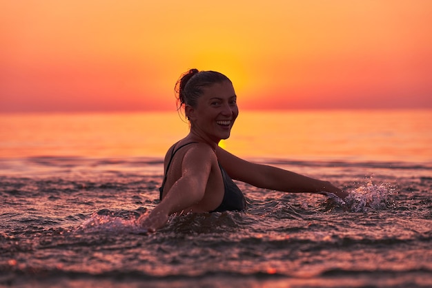 日の出の海で泳いでいる若い女性