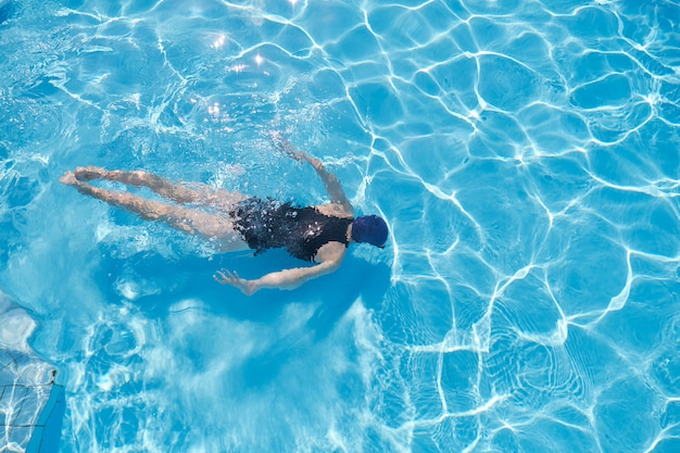 Foto giovane donna che nuota sott'acqua in una piscina all'aperto, vista dall'alto della parte posteriore della ragazza