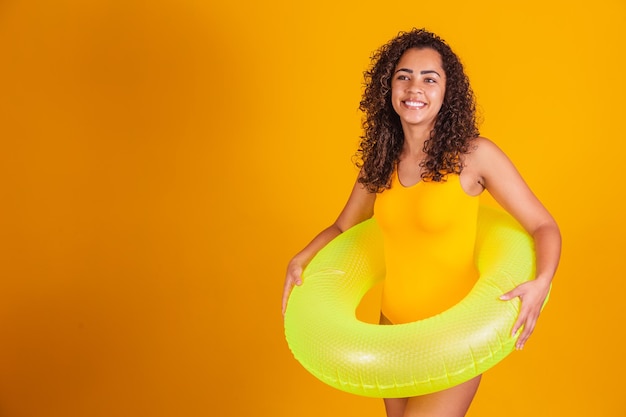 Young woman in swimsuit holding green float with happy face standing and smiling with confident smile showing teeth. Vacation and fun concept