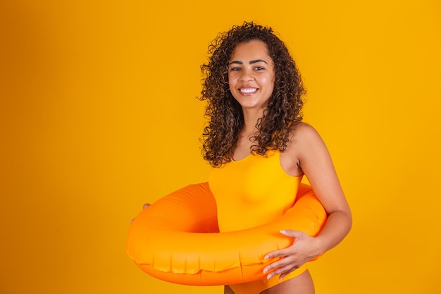 Young woman in swimsuit holding orange float with happy face standing and smiling with confident smile showing teeth. Vacation and fun concept