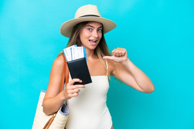 Young woman in swimsuit holding passport isolated on blue background proud and selfsatisfied