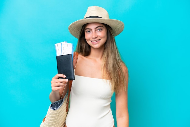 Young woman in swimsuit holding passport isolated on blue background smiling a lot