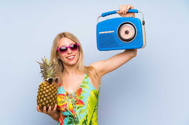 Young woman in swimsuit holding a pineapple with sunglasses and a radio