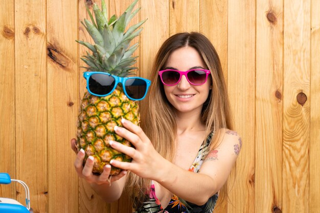 Young woman in swimsuit holding a pineapple with sunglasses