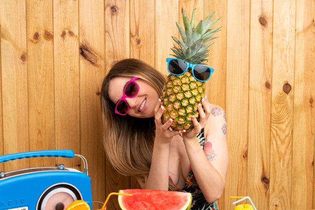 Young woman in swimsuit holding a pineapple with sunglasses