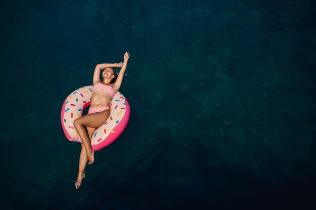수영복을 입은 젊은 여성이 바다에서 풍선 링 위에서 수영합니다. 여름 휴가 개념