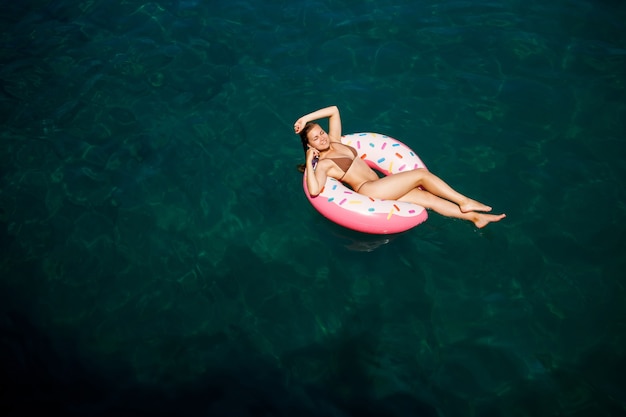 水着姿の若い女性が海の膨脹可能なリングで泳ぎます。夏休みのコンセプト。