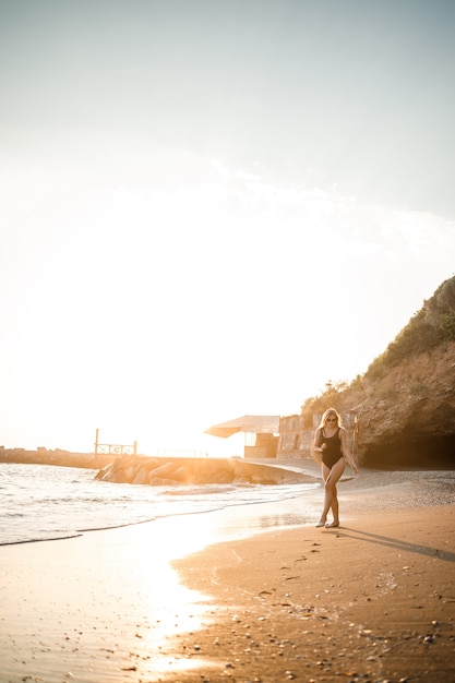 Young woman in a swimsuit with a beautiful figure on the seashore at sunset. Selective focus