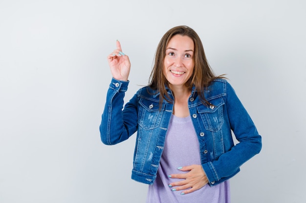 Young woman in t-shirt, jacket pointing up, looking away and looking merry , front view.