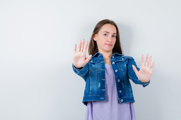 Tシャツを着た若い女性、停止ジェスチャーを示し、自信を持って見えるジャケット、正面図。