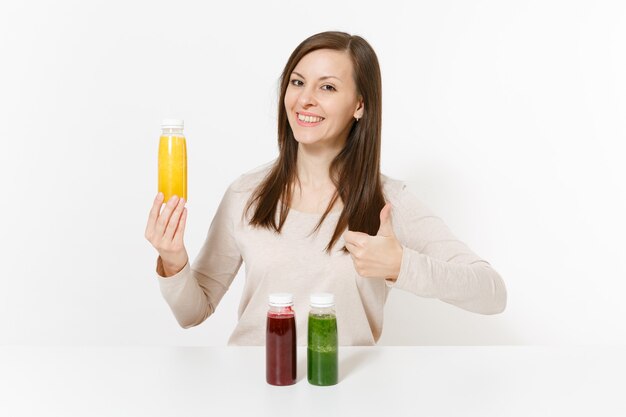 Young woman at table with green, red and yellow detox smoothies in bottles isolated on white background. Proper nutrition, vegetarian drink, healthy lifestyle, dieting concept. Area with copy space.