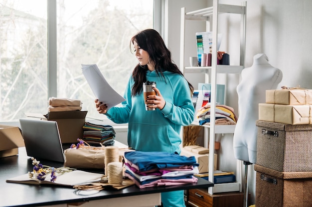 Young woman tailor fashion designer dressmaker using laptop in seamstress studio