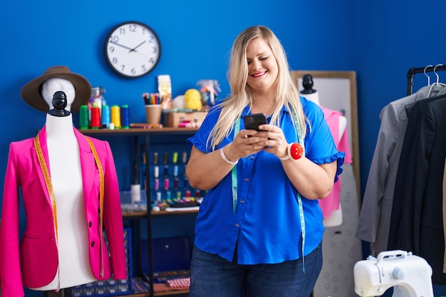 Young woman tailor smiling confident using smartphone at sewing studio