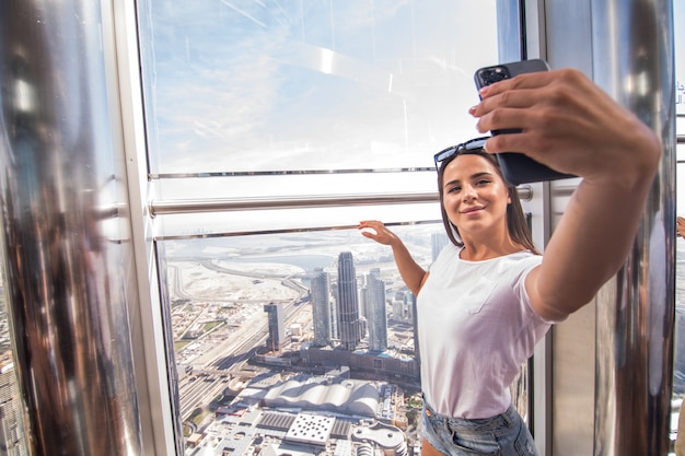 若い女性はブルジュハリファの上を歩きながら電話でselfieを取る