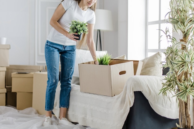 Young woman takes her favorite plants out of a cardboard box. moving to a new apartment