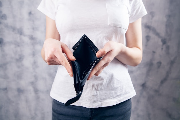 A young woman takes her wallet out of her pocket on a gray background