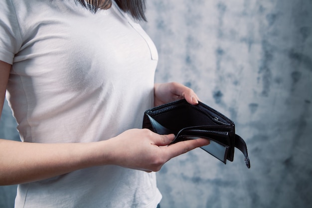 A young woman takes her wallet out of her pocket on a gray