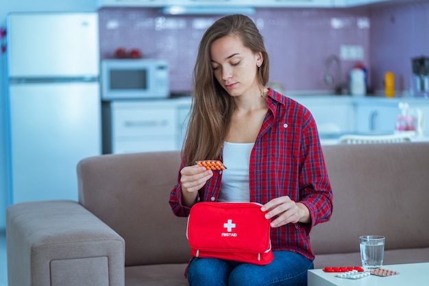 Young woman takes medicine at home. Medical first aid kit with pills from diseases and pains