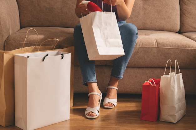 a young woman takes out her purchases from a bag while sitting on the sofa