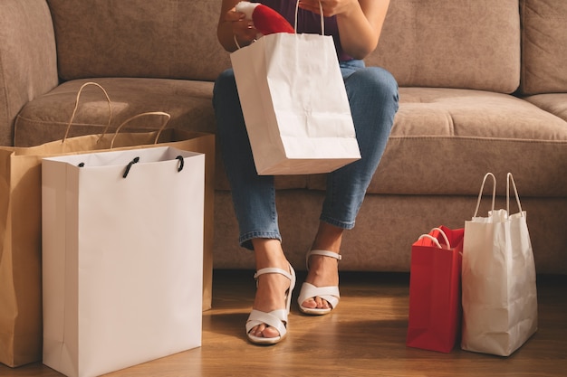 A young woman takes out her purchases from a bag while sitting on the sofa