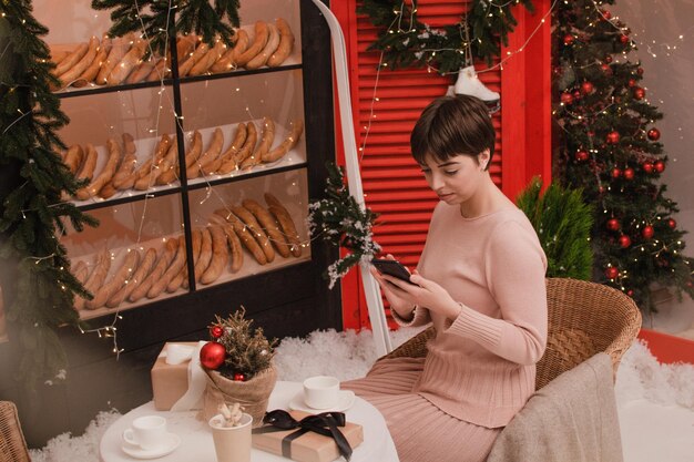 젊은 여자는 크리스마스 시간에 전나무 구성으로 축제 테이블에 사진 선물 상자를 가져옵니다