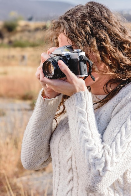 Young woman takes photos on her vacations, with retro photo camera in the field.