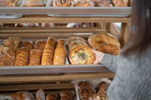 Young woman takes pizza from a wooden shelf with bread and baguettes in a supermarket Shopping and selection in the store Place for text