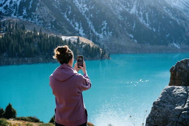 写真 雪山に囲まれた湖の写真を撮る若い女性