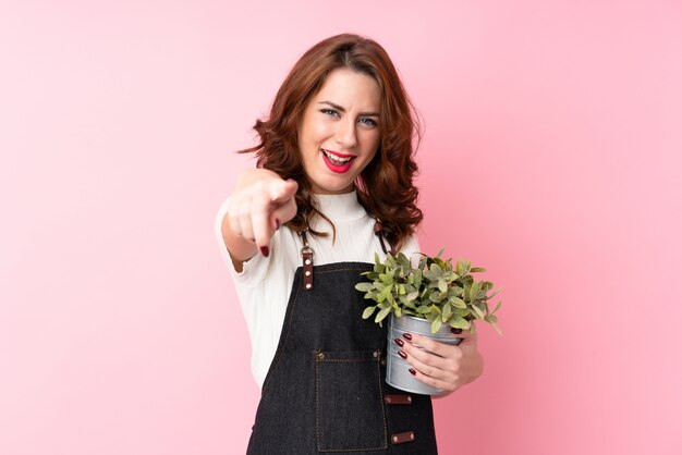 Young woman taking a flowerpot and pointing to the front