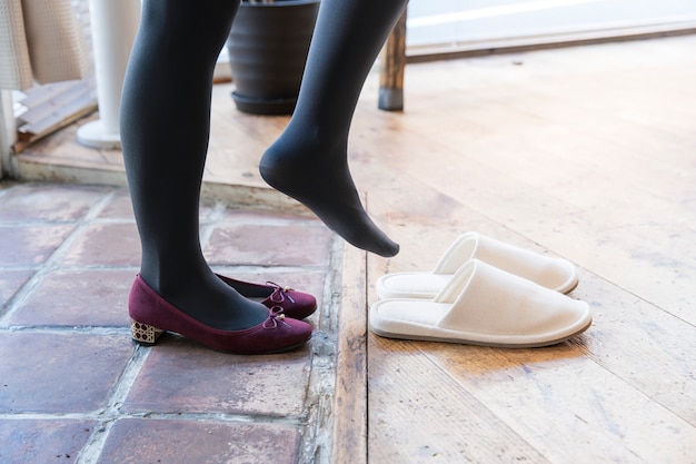 Young woman taking off her shoes and putting slippers on