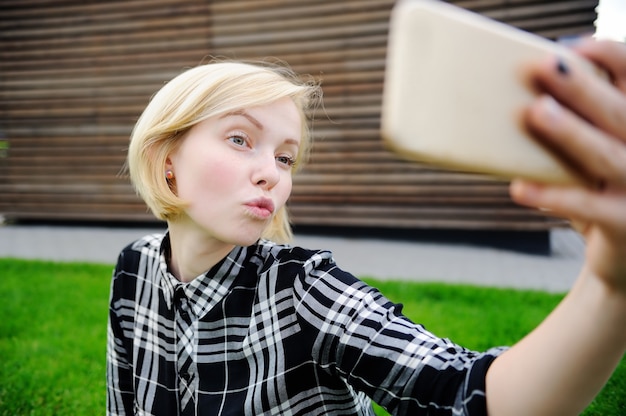 Молодая женщина, принимая Автопортрет на открытом воздухе (селфи) с смарт-телефона
