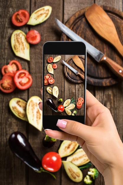 Foto una giovane donna che fotografa il cibo sullo smartphone, fotografando il pasto con la fotocamera mobile. realizzato per i social network. telefono cellulare con vista dall'alto