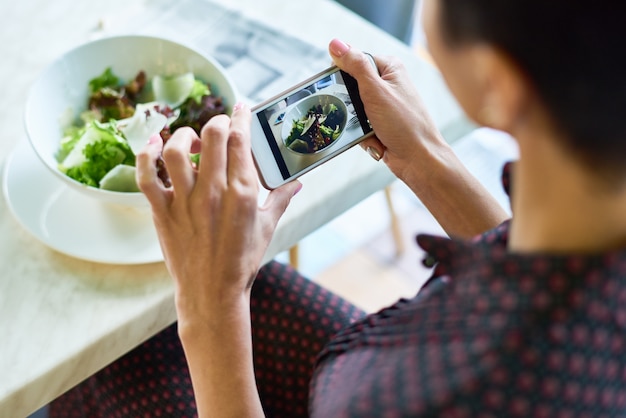 カフェでサラダの写真を撮る若い女性