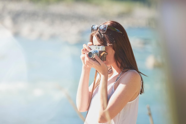 休暇中にデジタルカメラで自然の写真を撮る若い女性彼女のデジタルカメラを使用して川沿いの自然の風景の写真を撮る休日の冒険の若い女性