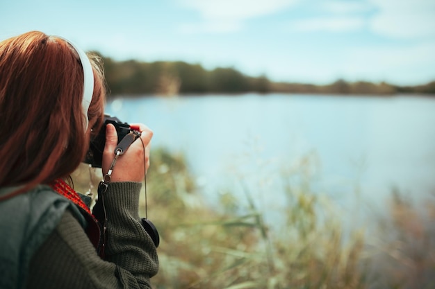 写真 古いアナログカメラで湖の近くで写真を撮っている若い女性