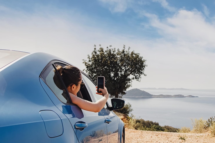Photo 車の開いた窓からスマートフォンで写真を撮る若い女性が道路のそばで立ち止まって眺めています