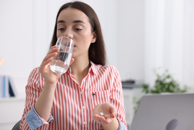 young woman taking pill against headache in office