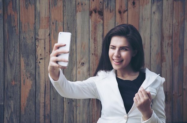 木製の壁に携帯電話からセルフィーを撮る若い女性