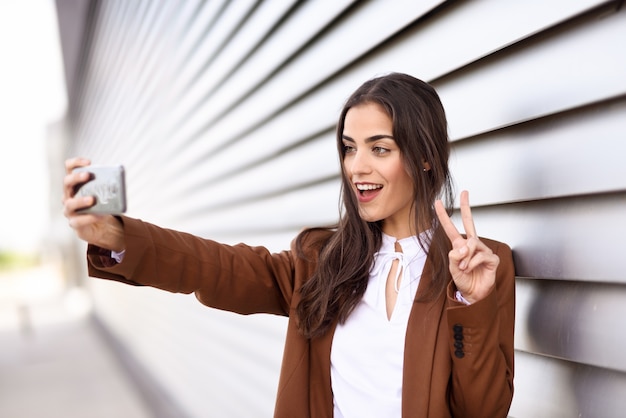 Young woman taking selfie photograph with smartphone doing V sig