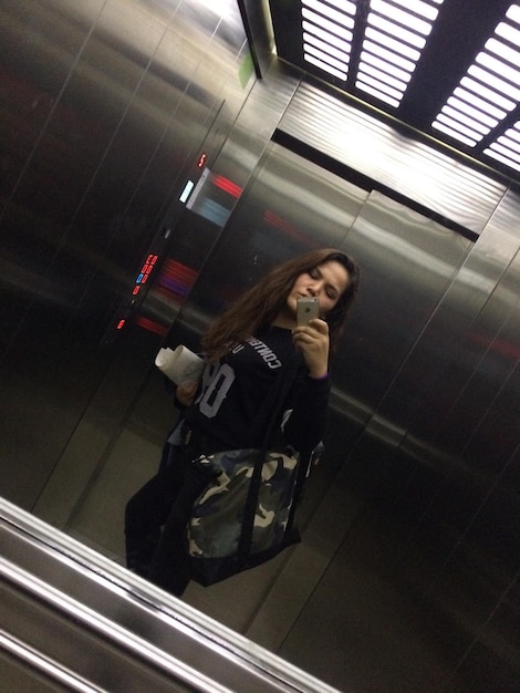 Photo young woman taking selfie reflecting on mirror in elevator