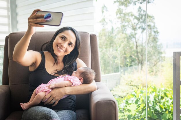 家で赤ちゃんと一緒にソファに座って自分撮りをする若い女性