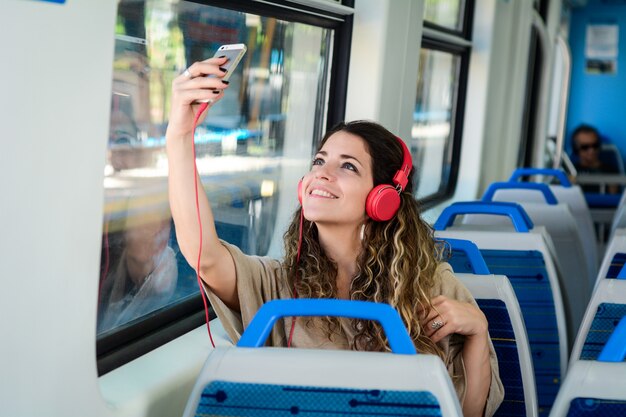 彼女の電話で電車の中でselfieを取っている若い女性。