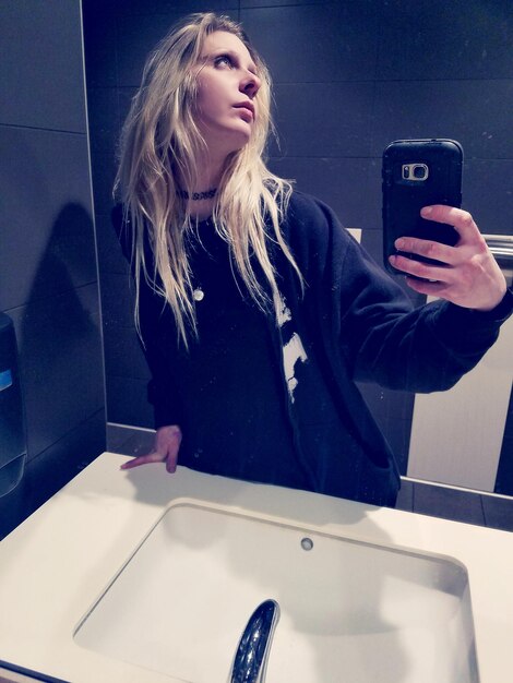 Young woman taking selfie with smart phone while standing in bathroom