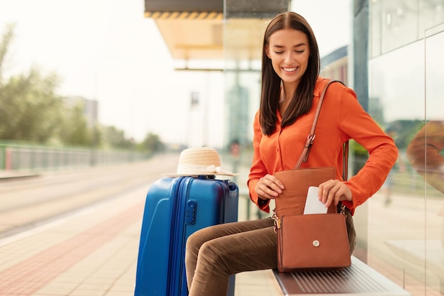 Young woman taking smartphone from handbag waiting at tram stop