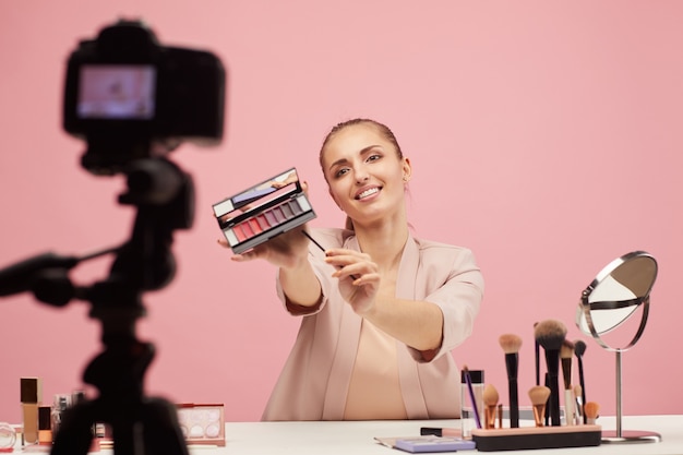 Young woman talking about decorative cosmetics and showing eyeshadows to the camera she making a beauty content