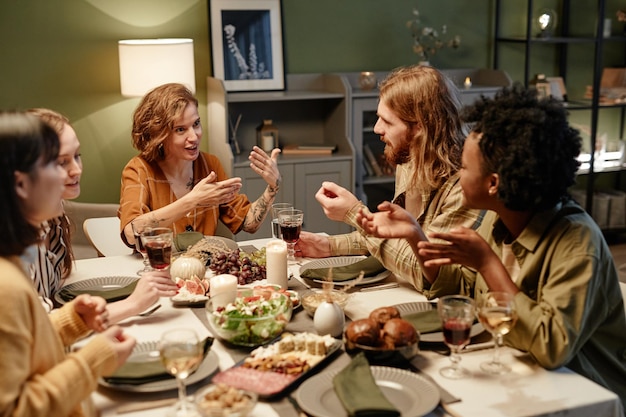 Photo young woman talking to her friends while they having a dinner at festive table in the living room