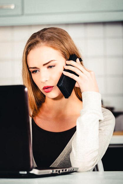 Photo young woman talking on mobile phone while using laptop at home