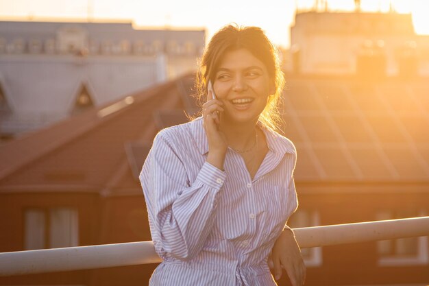 日没時にバルコニーで電話で話している若い女性