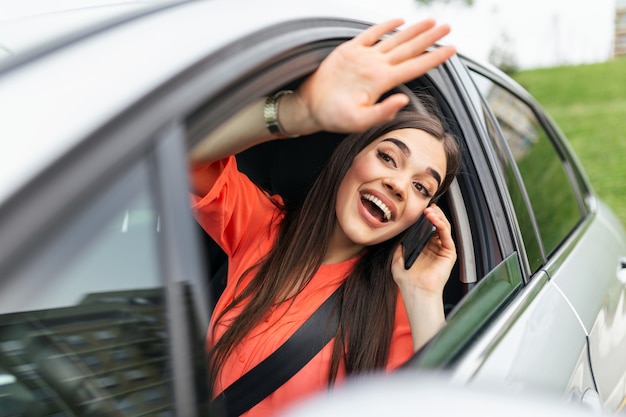 Young woman talking on the phone in the car and waving.